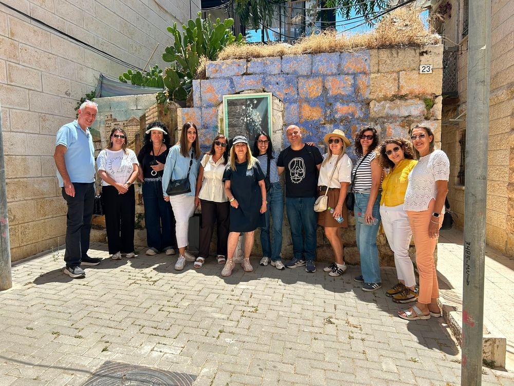 קבוצת תיירים מצטלמת יחד מול קיר אבן כפרי ביום שמשי.