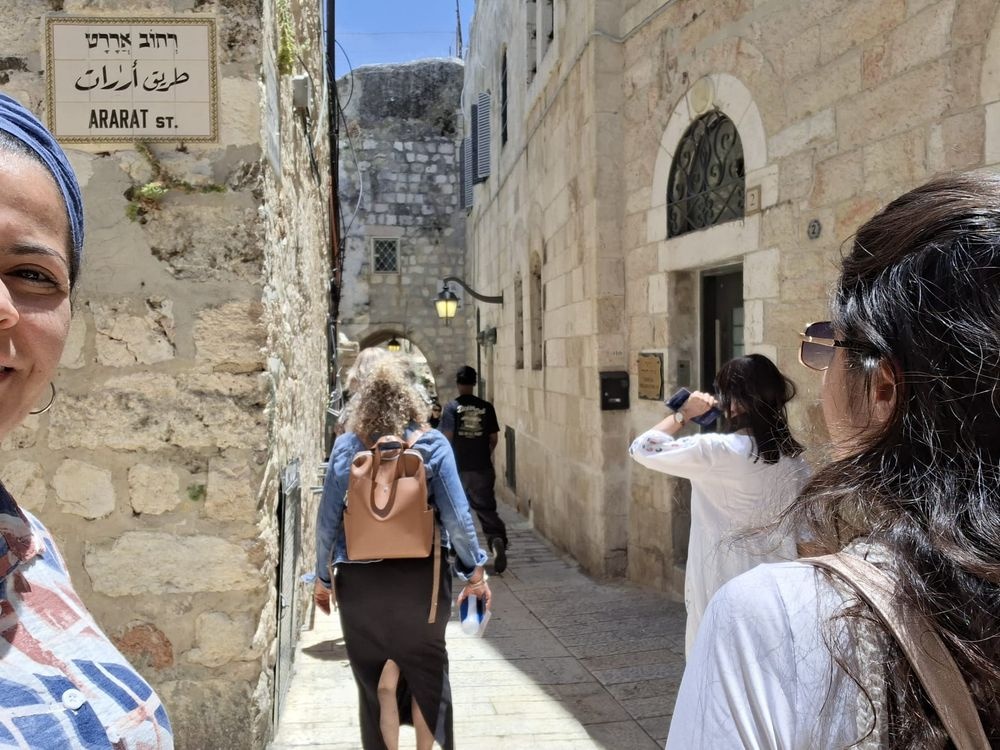 משתתפת מחייכת במסע המרכבה מרימה את ידה לצד פסל אדום בירושלים.