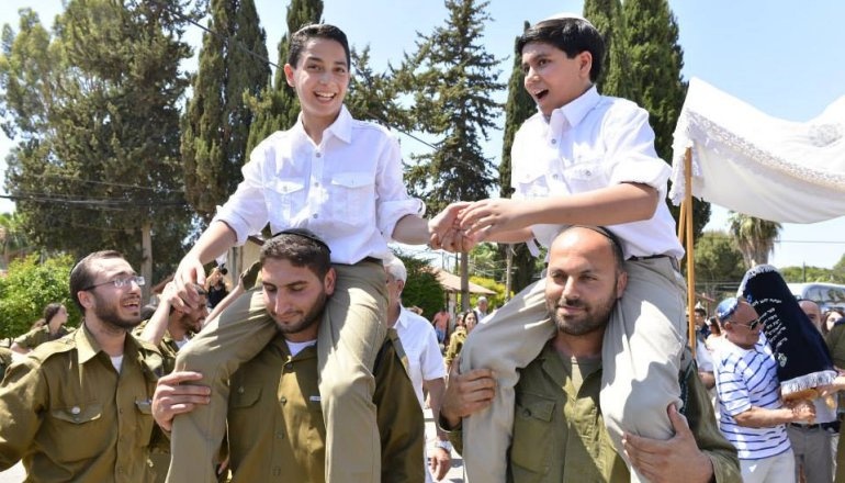 Celebrazione del Bar mitzvah a Gerusalemme con due ragazzi sollevati sulle spalle durante una processione tradizionale, circondati da familiari, amici e soldati.