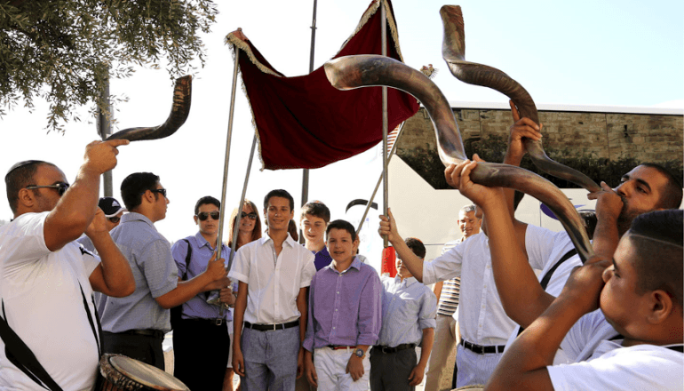 Celebrazione del Bar mitzvah in Israele con ragazzi sotto un baldacchino mentre i musicisti suonano gli shofar in una processione festosa.